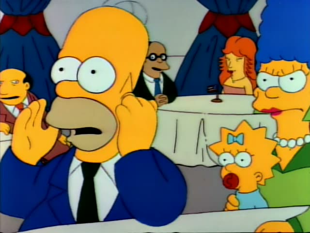 Homer sits at a restaurant table with a hand raised to his ear and a startled expression, while Marge in a green dress…