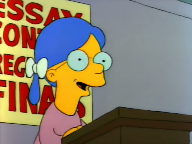 Milhouse stands behind a wooden podium in front of a yellow essay contest poster, speaking and gesturing with one hand…