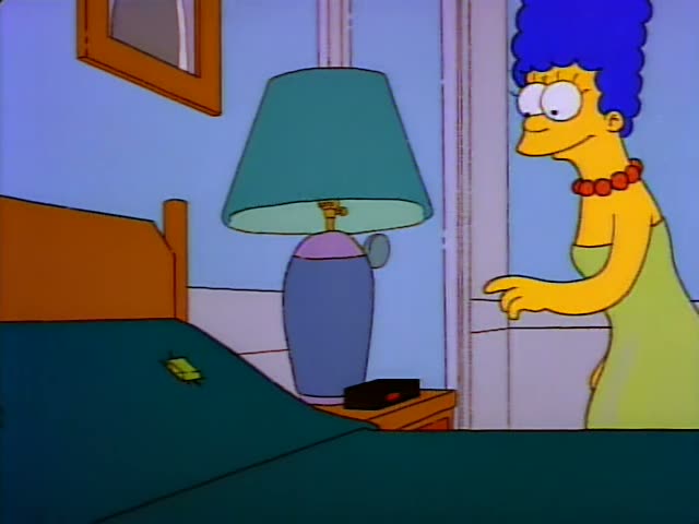 Marge Simpson stands at the doorway pointing while Homer Simpson sits on the edge of a green bed holding a reddish shoehorn