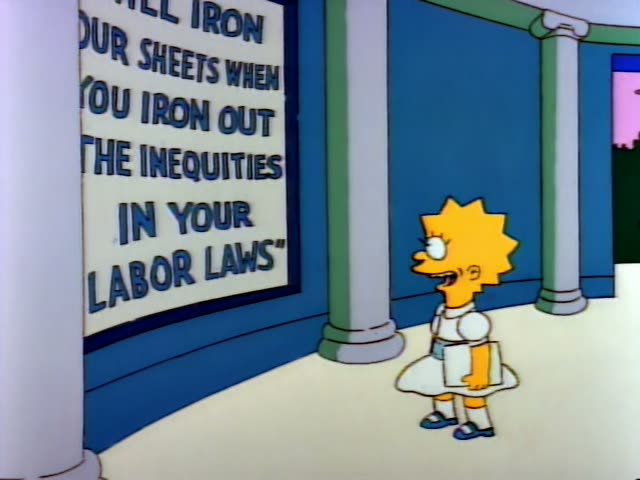 Lisa Simpson stands beside a wall sign…