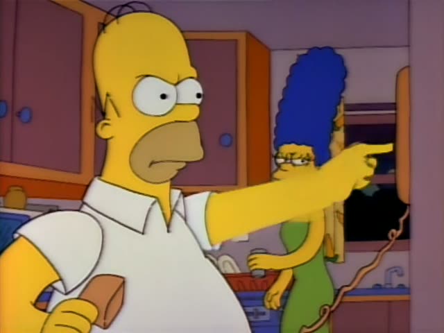 Homer Simpson and Marge Simpson stand in the orange-cabineted kitchen