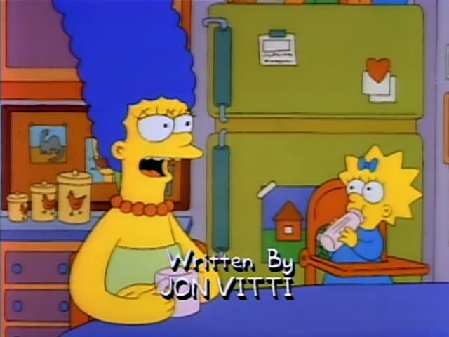 Marge Simpson stands in the kitchen holding a pink mug while Maggie sits in a high chair sucking on a bottle…