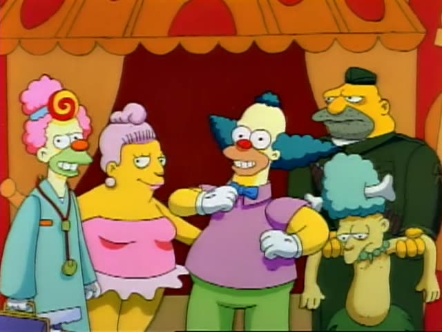 Krusty the Clown stands at the center of a group under an orange-and-red circus tent with a red curtain behind them…