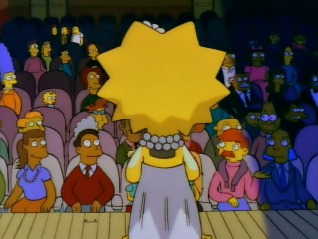 Lisa Simpson stands on a wooden stage and plays a large brass saxophone, first seen from behind and then in close profile…