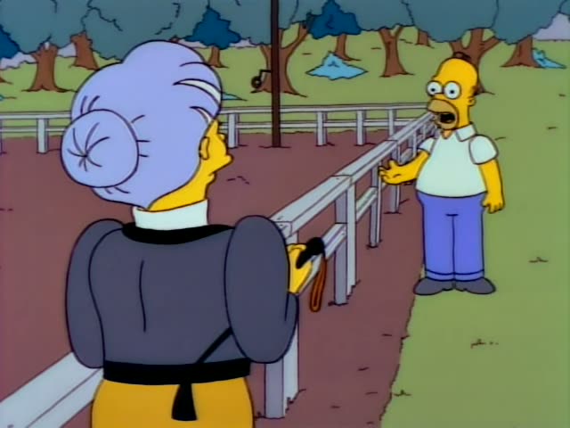 Homer stands on grass beside a white rail fence, gesturing with open hands and speaking, while a yellow-skinned woman…