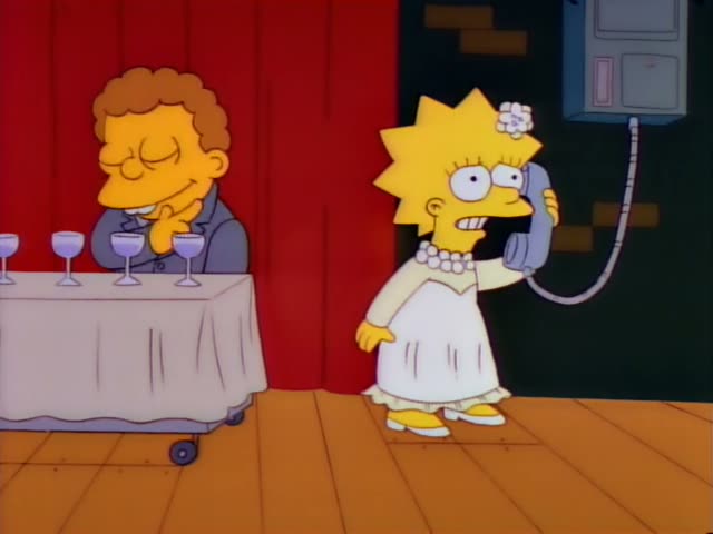 Lisa stands on a wooden floor by a wall phone, speaking into the receiver and gesturing with her free arm while a thin…