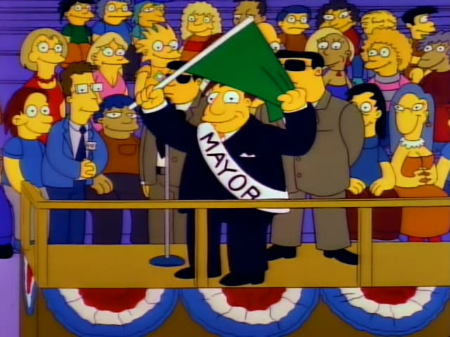Homer, Lisa, Maggie and Marge are seen in a crowd at a racing event while a mayor in a sash waves a green flag…