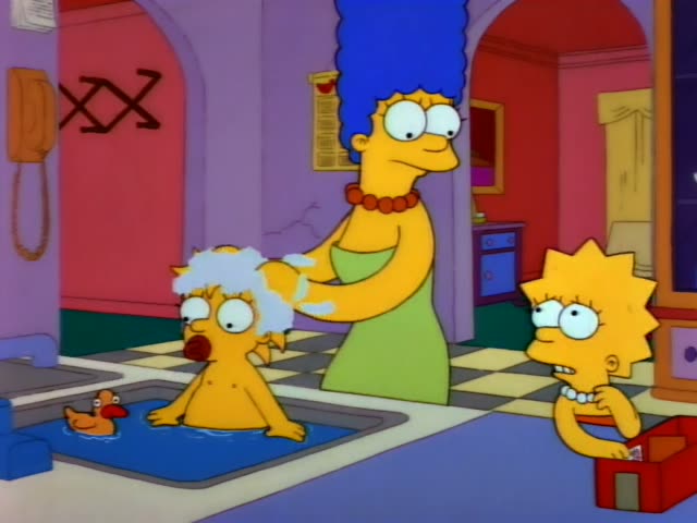 Marge Simpson stands beside a blue tub in the living room, washing the hair of a baby with white tufts who sits in the water…