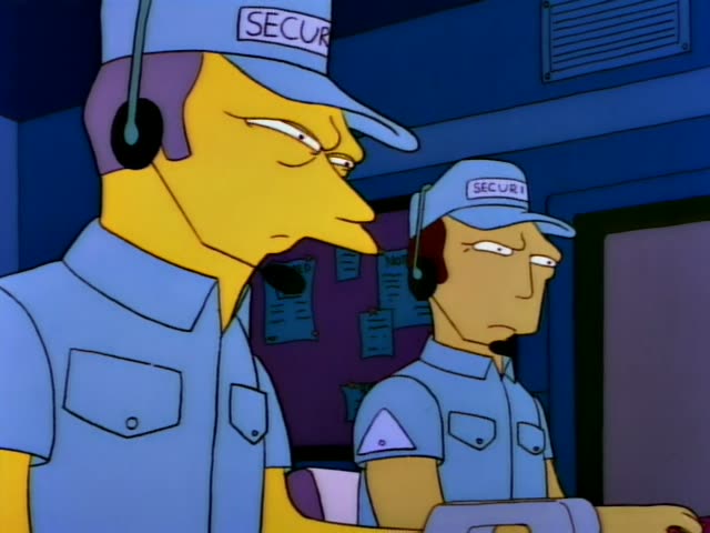 Two security guards in light blue uniforms and caps marked SECURITY stand with headsets in a blue-walled room, and one…