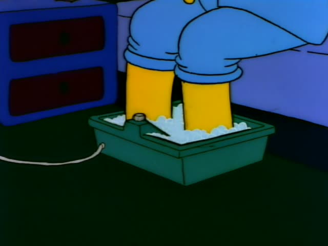 Homer sits at the kitchen dinner table while his bare yellow feet soak in a green tub of bubbly water on the floor…