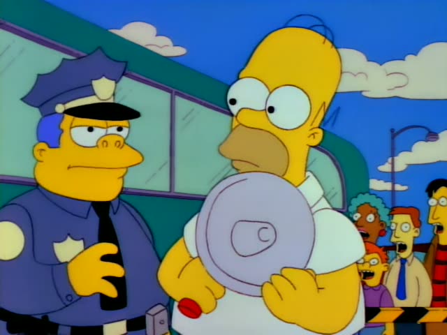 Chief Wiggum stands beside Homer Simpson outdoors in front of a green bus while a crowd of onlookers watches from the right