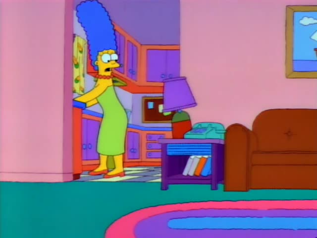 Marge Simpson stands in the doorway between the living room and kitchen, then rests her hands on her hips and looks…
