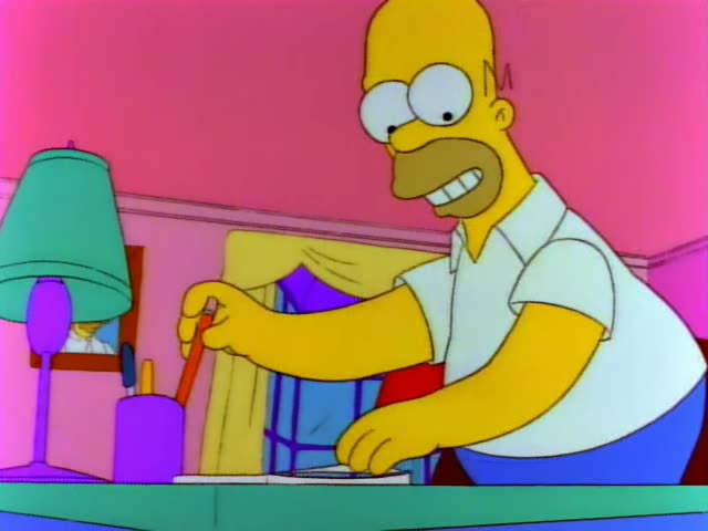 Homer Simpson stands at a green desk in a pink room beside a teal lamp, a purple pencil cup, and a framed picture on the wall