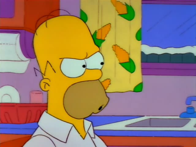 Homer stands in a kitchen beside Marge, who has a tall blue beehive, a red bead necklace and a pink top