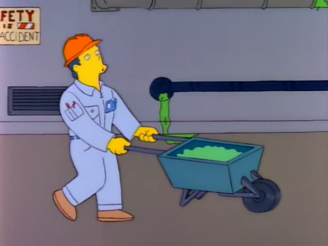 A heavy man in a white jumpsuit with an orange hard hat, who looks like Homer, pushes a teal wheelbarrow full of glowing…