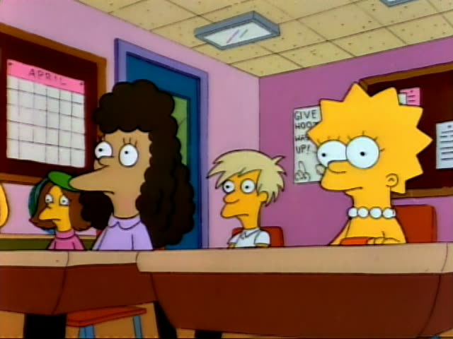 Lisa sits at a classroom desk next to a blond, spiky-haired boy in a white shirt and a curly-haired woman in a purple top…