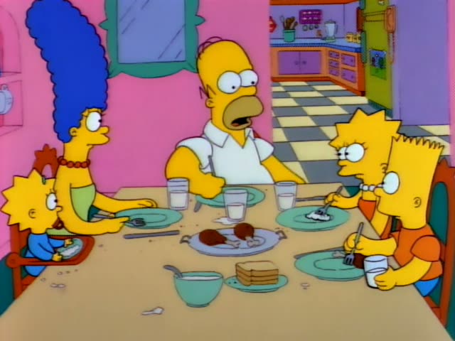 Homer Simpson sits at the dinner table in the pink kitchen, speaking with his mouth open while Marge Simpson sits beside him…