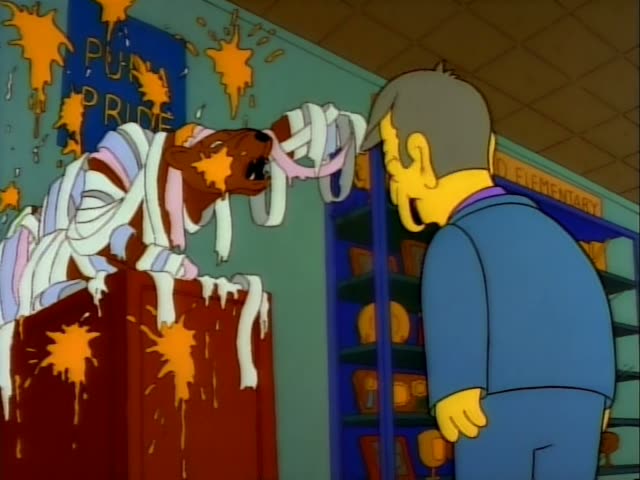 Principal Skinner stands in a school hallway beside a trophy case with an ELEMENTARY sign