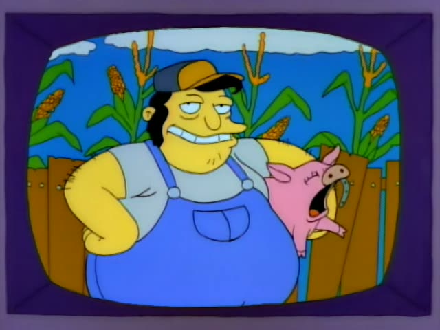A burly man in blue overalls and a yellow cap grins while holding a squealing pink pig beside a wooden fence with corn…
