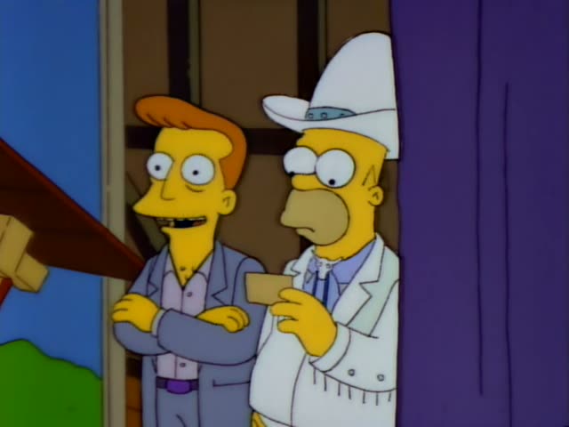 A thin, orange-haired man in a grey suit with crossed arms stands beside Homer, who wears a white cowboy hat and a white…