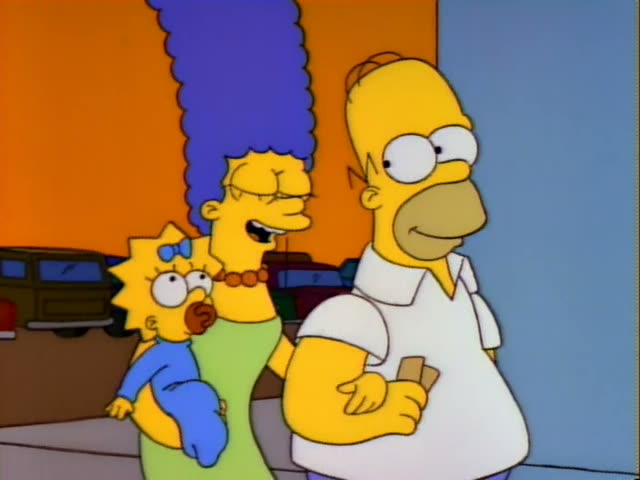 Homer, Marge and baby Maggie stand together on a sidewalk in front of a blue poster with large red lettering, with parked…