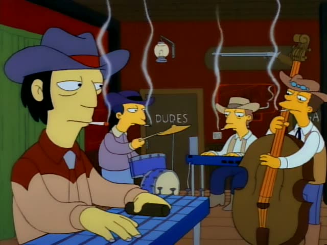 A cowboy-hatted man with a cigarette sits at a blue table playing a keyboard in a honky-tonk bar, while a drummer…