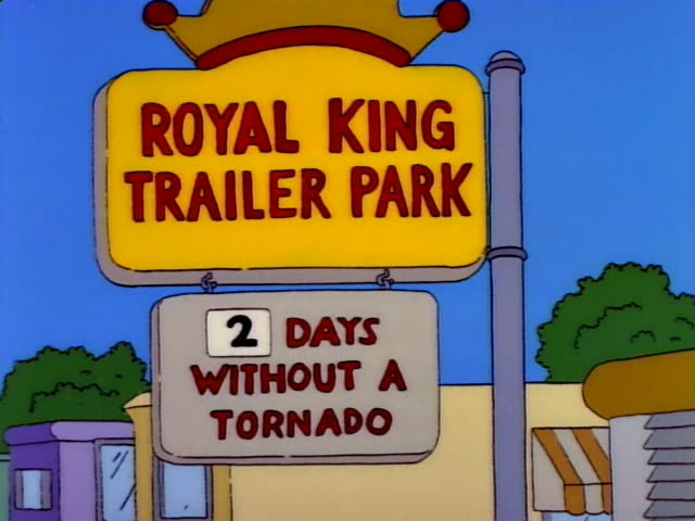 Homer embraces a blonde woman with a big bouffant hairdo, a blue headband, and an orange top outside the Royal King Trailer…