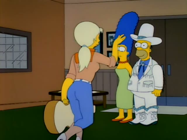Homer stands beside Marge, who has a tall blue beehive, a green dress and a red bead necklace, while a blonde woman…