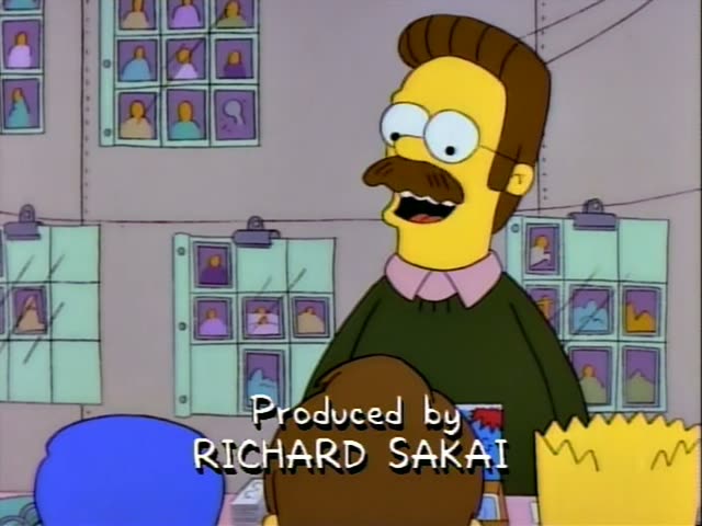 Ned Flanders stands before a wall of framed photos while Bart, in his orange shirt, Nelson and Milhouse stand together…