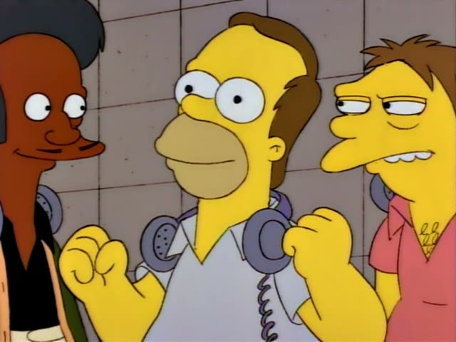 Apu stands at left with a headset around his neck beside a brown-haired man in a white shirt with headphones around his neck…