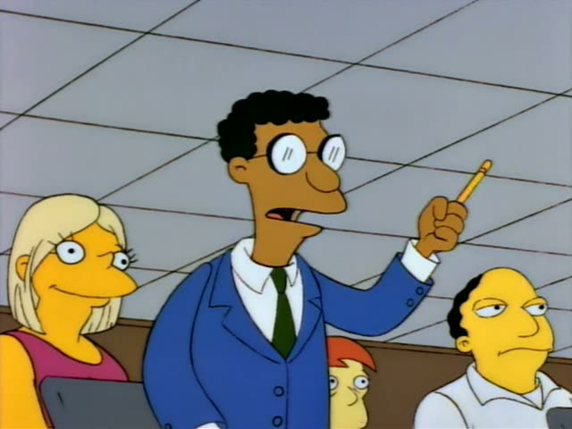 Carl raises a pencil in a crowded seminar room beside a blonde woman in a pink top and a dark-haired man in a white shirt