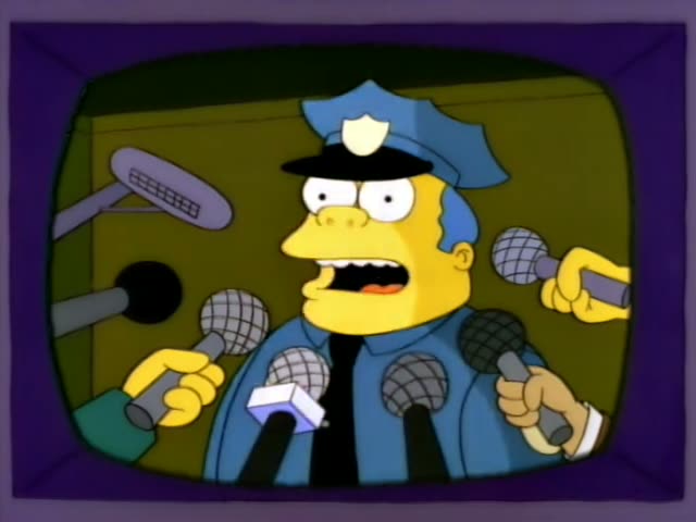 Chief Wiggum stands before a bank of microphones, grimacing and then looking worried as reporters hold them up to him