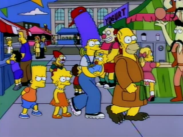 Bart, Lisa, Marge holding baby Maggie, and Homer in a long brown robe with a green belt walk together along a fairground…