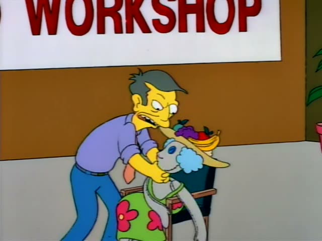 A grey-haired man in a purple shirt and orange tie wrestles with a ragged doll-like figure with blue hair…