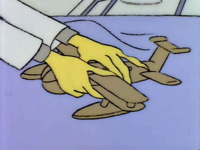Mr. Burns sits up in a bed while yellow-gloved hands set a wooden model airplane on the blanket