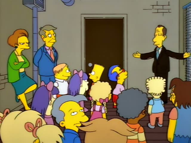 Milhouse stands in front of a thin man in a dark suit and light blue tie, while Bart in his orange shirt and blue shorts…
