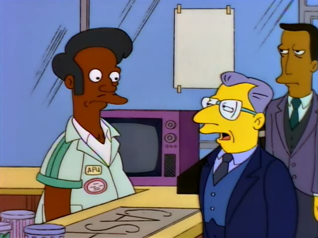 Apu stands behind the counter beside a bespectacled man in a dark suit and blue vest with purple-grey hair, while a taller…