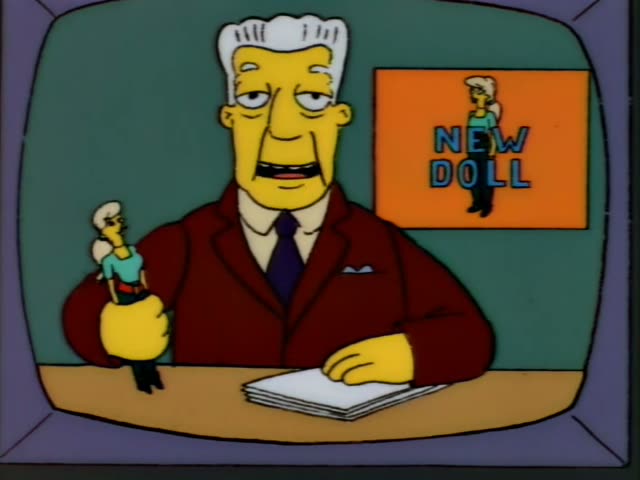 Kent Brockman sits at a news desk in front of a green backdrop and an orange "NEW DOLL" sign showing a doll