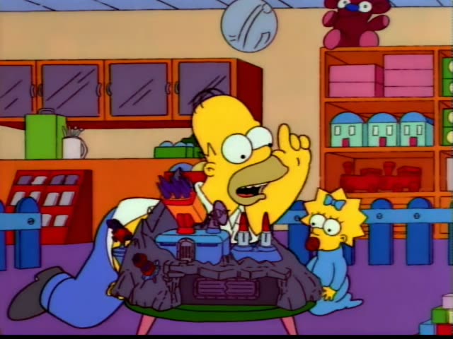 Homer Simpson gestures and talks while Maggie Simpson sits nearby watching him at a low round table holding a toy…