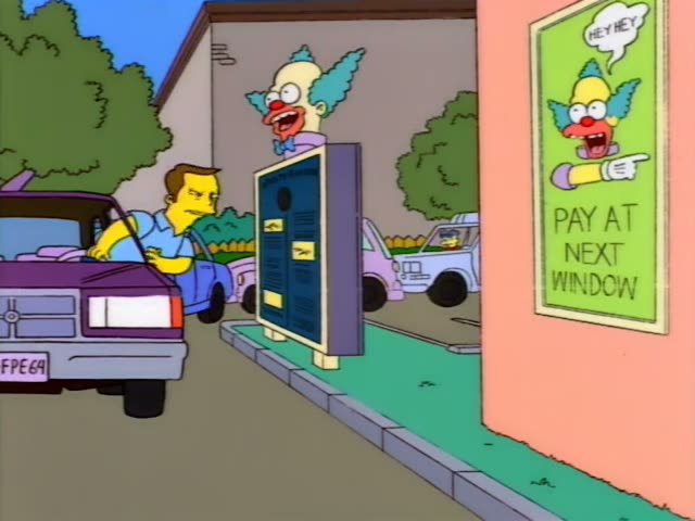 Krusty the clown's face peeks over a drive-thru speaker box beside a sign reading PAY AT NEXT WINDOW, as a man in a blue…