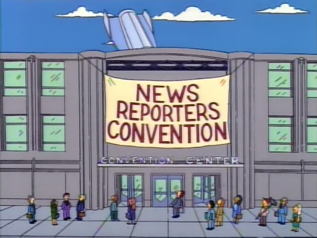 Homer Simpson sits in a hatch window beside a dark-haired astronaut and a grey-haired astronaut with a US flag patch…