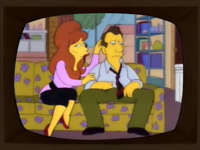 A woman with a tall red beehive, pink top and black skirt sits close beside a man with brown hair, a light blue shirt…