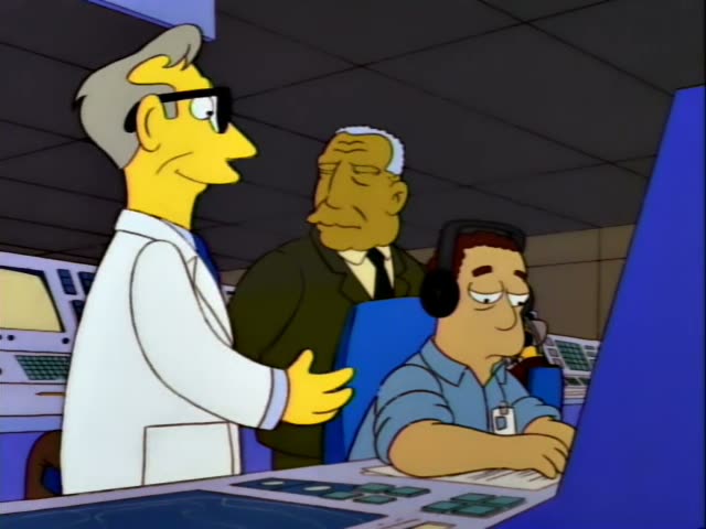 A man in a white lab coat with grey hair and glasses stands beside an older man in a dark green suit and a seated man…