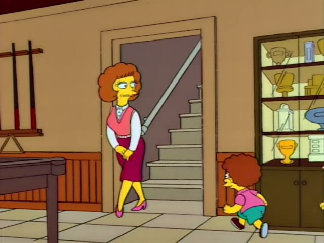 A woman with orange curly hair, a pink vest and a maroon skirt stands in a room with a pool table, a glass trophy cabinet…
