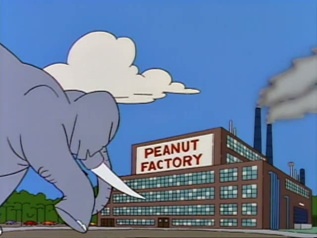 Homer spreads his arms in a doorway of the Peanut Factory as a grey elephant with tusks walks toward the building…