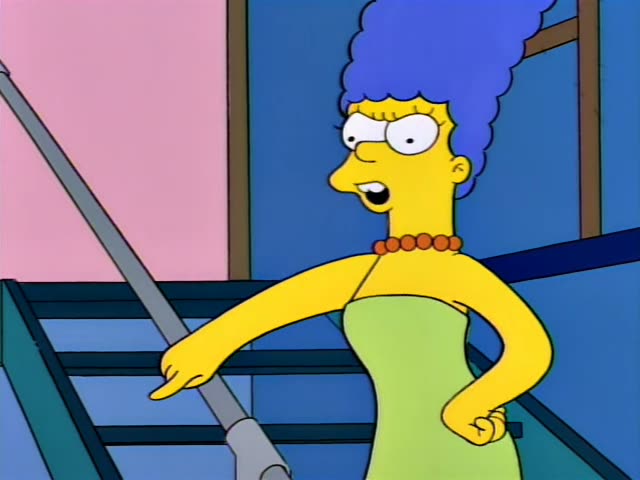 Marge Simpson stands with one hand on her hip in a blue room beside a metal railing and a teal staircase