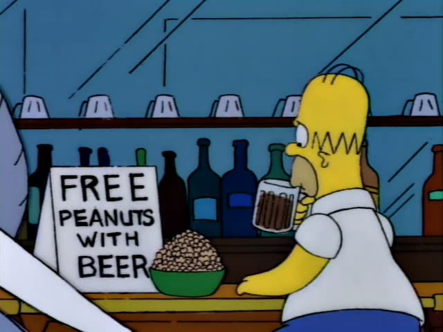 Homer Simpson sits on a red-cushioned barstool, holding a mug of beer beside a green bowl of peanuts and a sign reading FREE…