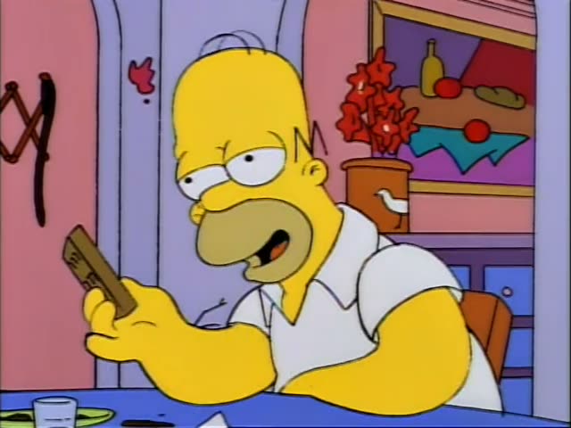 Homer sits at a blue table in a pink-walled room holding a small brown booklet and reading it, then looks up and turns away…