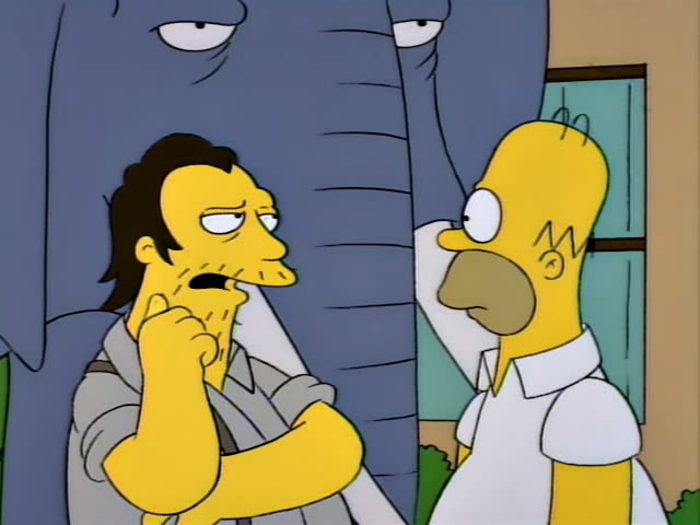Homer Simpson stands beside a stubbled man with slicked-back dark hair and a grey jacket, who is arms-crossed with one hand…