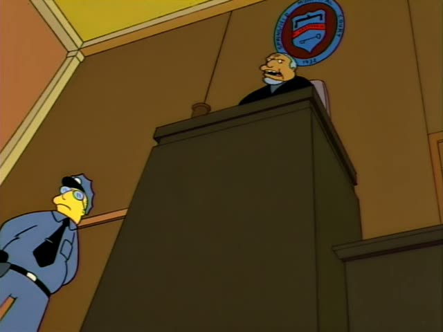 Homer and Marge Simpson sit side by side at a courtroom table while Troy McClure holds up a shoe and a small hammer-like…